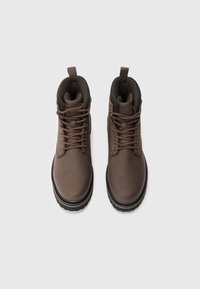 Botas de cuero marrón con cordones, con cuellos acolchados y lengüetas para tirar, exhibidas una al lado de la otra sobre un fondo blanco liso.
