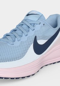 Ανοιχτό μπλε αθλητικό παπούτσι Nike με ροζ σόλα και μαύρο λογότυπο swoosh, με διχτυωτό επάνω μέρος και κορδόνια.