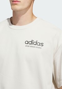 Light beige crewneck sweatshirt in soft cotton blend, featuring a black printed logo 'adidas SPORT DESIGN STUDIO' on the chest.