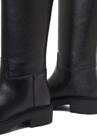 Schwarze kniehohe Lederstiefel mit strukturierter Oberfläche, flachen Gummisohlen und Ziernähten entlang der Kanten.