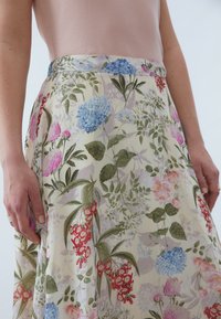Long floral skirt featuring a pale background with pink, red, and blue flowers. The fabric is soft with a flowing design and subtle sheen.