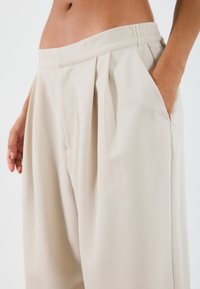 Pantalons larges couleur beige clair en tissu lisse, dotés de plis, d'une taille élastique et de poches latérales.