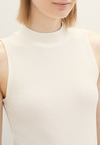 Top senza maniche in bianco sporco, caratterizzato da un collo alto e una texture morbida. Progettato per un look aderente con sottili linee verticali.