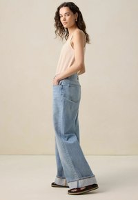 Jean large bleu clair à taille haute, avec deux poches latérales et un ourlet retroussé. Associé à un haut à bretelles rayé beige.