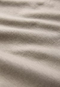 Ljus beige textil med en slät yta, som har subtila ribbade mönster och mjuka veck, vilket skapar djup och ett mjukt utseende.