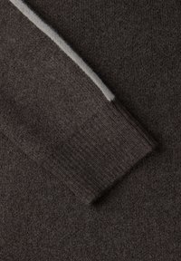 Detal włóczki brązowego swetra pokazujący fakturę tkaniny, ściągacz na mankiecie oraz kontrastowy jasnoszary pasek wzdłuż szwu rękawa.