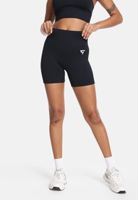 Crne sportske kratke hlače s visokim strukom, glatke teksture i malim bijelim logotipom s lijeve strane. Nosite ih s bijelim čarapama i tenisicama.