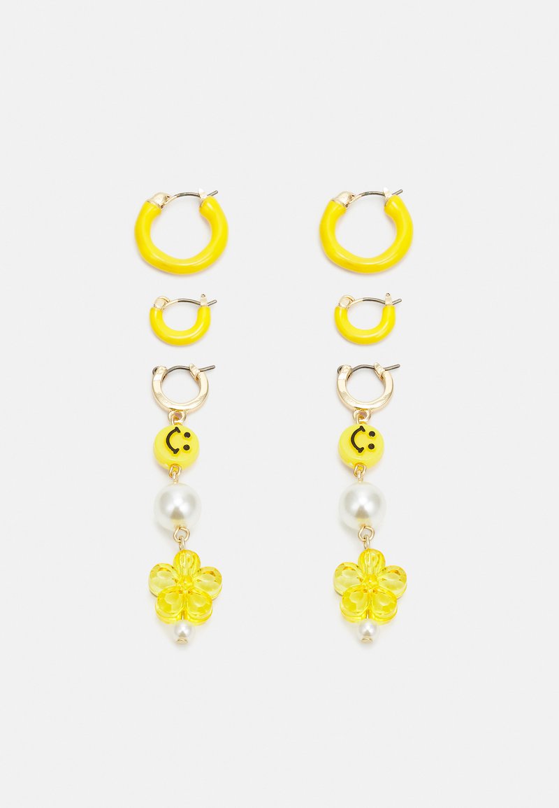 Brincos em forma de aro amarelos com textura suave, apresentando aros menores, contas sorridentes, detalhes em pérola e charms florais.