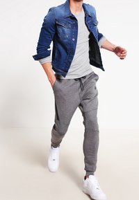 Jeansjacka i blå ton, grå figursydd t-shirt och grå joggers med detaljer på sidopanelerna, komplett med vita sneakers.