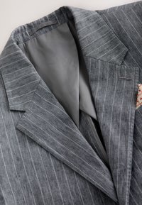 Blazer a righe grigie realizzato in tessuto strutturato, con colletto a revers e fodera grigia. Include un piccolo fazzoletto decorativo nel taschino.