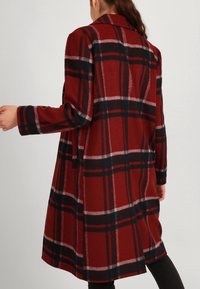 Cappotto a quadri rosso e nero con maniche lunghe, colletto e vestibilità ampia. Realizzato in tessuto morbido, presenta strisce orizzontali e verticali.