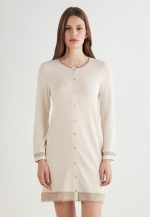 Beige långärmad klänning med rund halsringning, knäppningar framtill och vågformig spetsdetalj vid ärmar och nederkant. Mjuk, slät tyg.