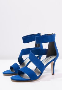 Sandali alti in suede blu con tre cinghie davanti e una cinghia alla caviglia, tacco beige, punta aperta e zip sul retro.