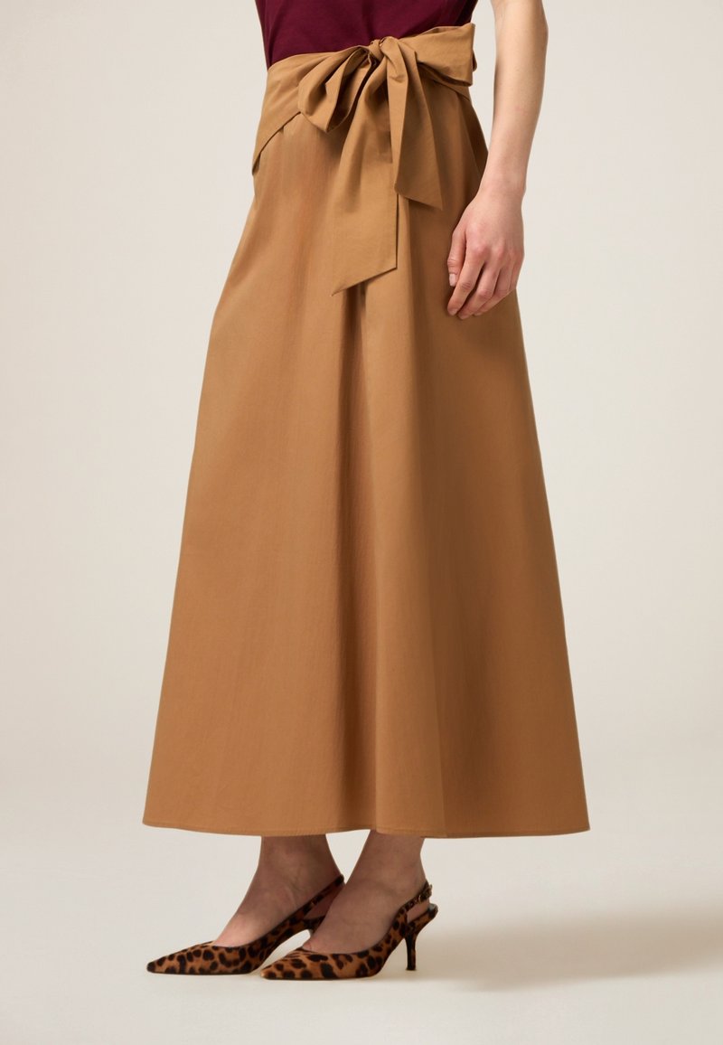 Larga falda de color topo con un lazo en la cintura, combinada con tacones tipo slingback de estampado de leopardo. La tela parece suave y estructurada.