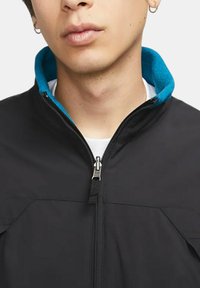 Svart jacka med dragkedja fram, med en turkos fleece-krage och en slät yta. Inkluderar två vinklade framfickor.