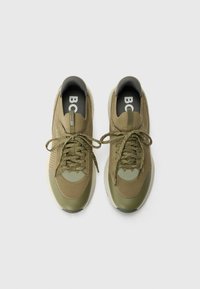 As sapatilhas verde-oliva apresentam um cabedal em malha, detalhes texturizados, bico redondo e atacadores em contraste, com um colarinho acolchoado cinza e logotipo.