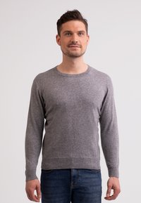 Grauer Strickpullover mit langen Ärmeln, Rundhalsausschnitt und gerippten Bündchen und Saum, kombiniert mit blauen Jeans. Glatte Textur, minimalistisches Design.