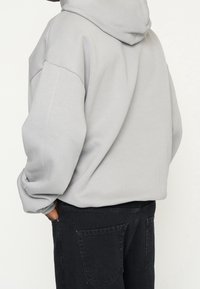 Jasnoszara bluza z kapturem o luźnym kroju, z ściągaczami przy rękawach i bocznymi szwami. Połączona z czarnymi, miękkimi spodniami.