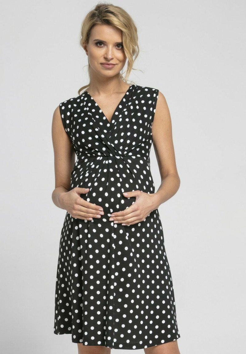 Black polka dot dress with a wrap design, short sleeves, and a fitted bodice. The fabric is smooth, and the dress flows to the knee.