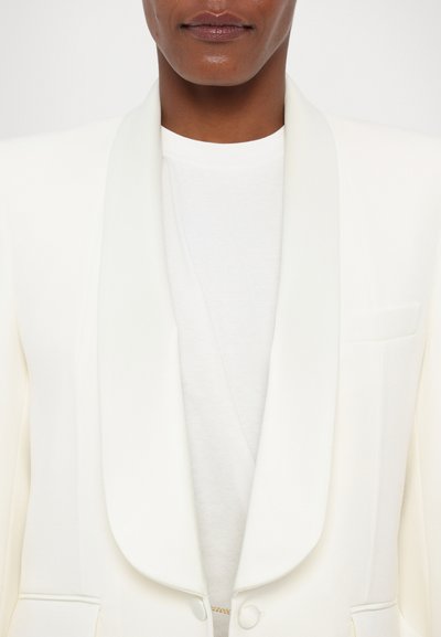 Witte blazer met een gladde stofafwerking, sjaalkraag, sluiting met een enkele knoop en een subtiele zakdetail, gedragen over een wit top.
