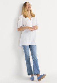 Valkoinen, lyhythihainen tunika V-pääntiellä, yhdistettynä vaaleansinihin leveälahkeisiin farkkuihin ja samanvärisiin loafer-kengiin. Pehmeä kangas rentoon istuvuuteen.