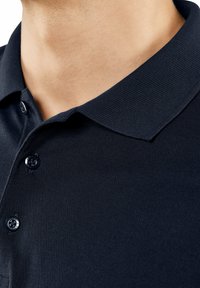 Granatowa koszulka polo z teksturowanej tkaniny, z złożonym kołnierzykiem i dwoma guzikami na listwie. Zbliżenie ukazujące szczegóły kołnierzyka i górnej części tkaniny.