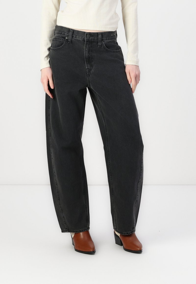 Black, high-waisted jeans with a loose fit; features five pockets and subtle stitching details along the seams. Paired with brown heeled shoes.