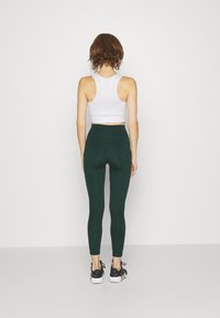 Vit sportig crop top kombinerad med högmidjade mörkgröna leggings. Tyget verkar vara slätt med en tajt design. Svarta sportskor fulländar looken.
