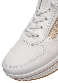 Nærbillede af hvid lædersneakerspids med teksturerede hvide snørebånd og metalisk gylden sideliste på gummisål.