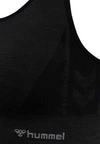 Brassière de sport noire Hummel en tissu sans couture, motifs texturés et logo sur la bande élastique sous la poitrine.