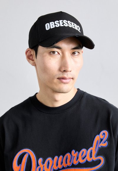 Cappellino da baseball nero con testo bianco "OBSESSED2", abbinato a una felpa nera con ricamo colorato "Dsquared2".