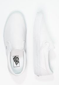 Bílé plátěné nazouvací boty s texturovanou gumovou podrážkou a elastickými bočními detaily. Na stélce je logo Vans. Minimalistický design.