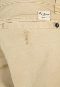 Beżowe dżinsy o gładkiej fakturze, z tylną kieszenią i wplecioną metką z napisem "Pepe Jeans London Since 1973".