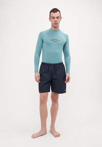 Világos türkiz színű, hosszú ujjú rash guard, középkori logóval, sötét tengerészkék fürdőnadrággal párosítva, amely elasztikus derékpánttal és logó kiemeléssel rendelkezik.