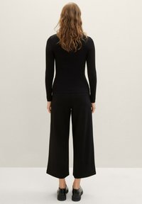 Top nero a costine con maniche lunghe abbinato a pantaloni neri a gamba larga. Texture liscia con una silhouette aderente e un design dei pantaloni rilassato.