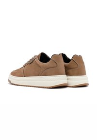 Zapatillas de ante marrón con parte superior texturizada, cordones redondos y suela de goma blanca en contraste. Presentan un diseño minimalista y acentos cosidos.