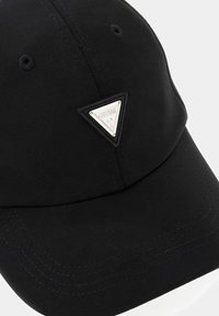 Casquette noire en tissu doux avec un patch logo métallique triangulaire à l'avant, détails cousus et visière incurvée.