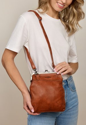 Brun læder crossbody taske med en sølvfarvet metal spænde, justerbar rem og en struktureret overflade. Har et brandlogo på forsiden.