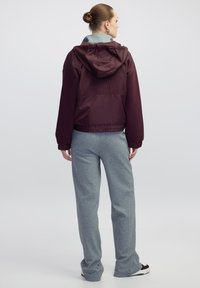 Chaqueta con capucha burdeos de textura fruncida, combinada con pantalones de chándal grises. La chaqueta cuenta con puños elásticos y un dobladillo corto para un aspecto ajustado.