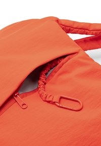 Élénk narancssárga hátizsák szövet sima textúrával, cipzáras zsebbel és összegyűrt szegéllyel. Tartozik hozzá egy hozzáillő karabiner csipesz is.