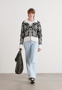 Sweter z dzianiny w czarno-białym geometrycznym wzorze, z zamkiem z przodu i ściągaczem na dolnym brzegu. Połączony z jasnoniebieskimi dżinsami i czarną torebką.