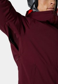 Bordeaux ski-jack met een hoge kraag, ventilatieopeningen en subtiele textuur. Voorzien van een ritszak aan de zijkant voor extra gemak.