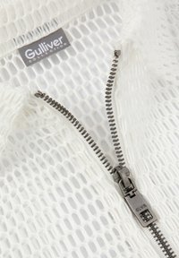 Veste en maille blanche avec une fermeture éclair argentée et une étiquette de marque "Gulliver Collection" près du col. Design texturé et respirant.