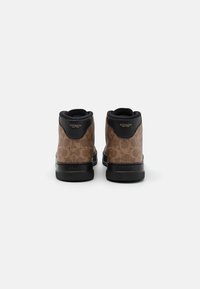 Bruine hooggekraagde sneakers met een patroon, zwarte leren accenten, rubberen zolen en gouden branding op de hak, gezien van de achterkant.