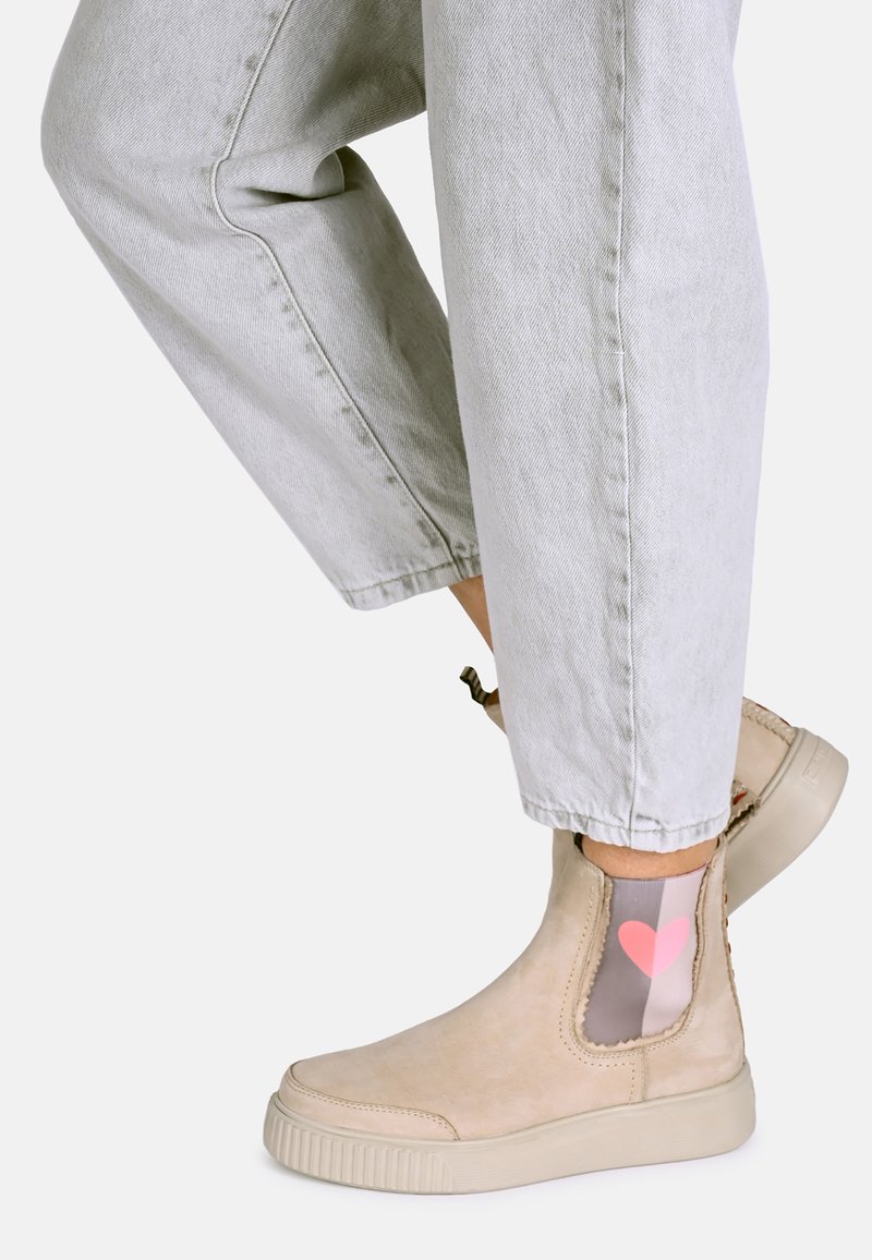 Beżowy botek za kostkę z elastycznym boku, teksturowanym zamszowym wierzchem, okrągłym noskiem i jasną podeszwą. Skarpeta ma wzór serca w kolorze różowym.