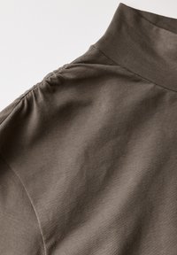 Tummanruskea paito, jossa on korkeakaulainen malli, pehmeä ribbitekstuuri, kerätty yksityiskohta hartiasaumojen kohdalla ja sileä kangaspinta.