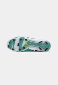 Football cleat featuring a translucent white sole with green accents, black rubber studs, and a yellow Nike logo near the heel.
