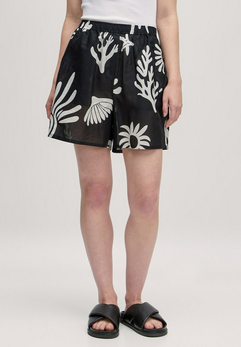 Shorts noirs avec un motif de corail et de fleurs blanches, ceinture élastique et tissu léger, associés à des sandales noires.
