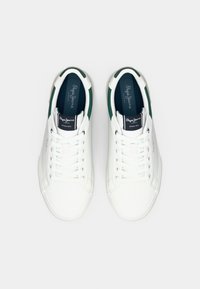Zapatillas blancas con un material sintético suave, detalles verdes en el talón y un diseño clásico de cordones. Logotipo notable en la lengüeta.