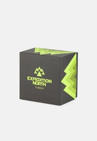 Boîte noire avec un design en zigzag vert et le logo "EXPEDITION NORTH TIMEX" à l'avant, présentant une texture lisse et mate.